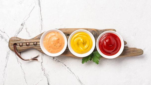 Top view of yellow mustard, red ketchup and paprika sauce in small bowls on white marble background - Foto, Bild