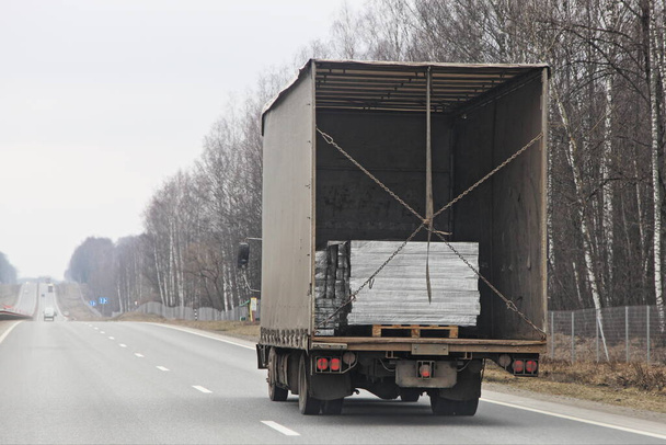 Camion fourgon avec porte arrière ouverte transporte des palettes sur la route de banlieue au printemps sur fond de forêt, cargaison de livraison erronée
 - Photo, image