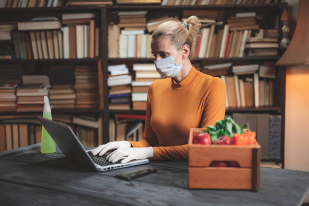 Жінка з захисною маскою від вірусів і патогенів, використовуючи ноутбук вдома, замовляючи їжу, продукти харчування, припаси через Інтернет
. - Фото, зображення