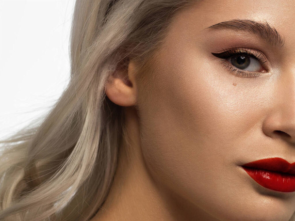Close-up beauty of half female face with creative fashion evening make-up. Black arrows on the eyes and extremely long eyelashes, on full red lips matte scarlet lip color. Well-groomed skin after spa - Foto, Imagem