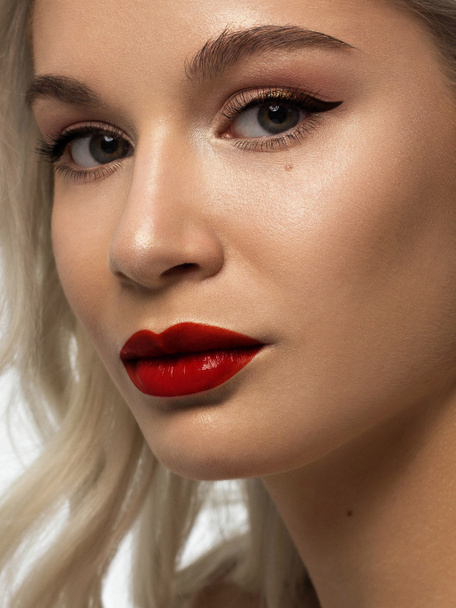 Close-up beauty of a female face with fashion evening make-up. Black liner on the eyes and extremely long eyelashes, on full lips matte scarlet lip color. Well-groomed skin after spa. red lipstick - Foto, imagen