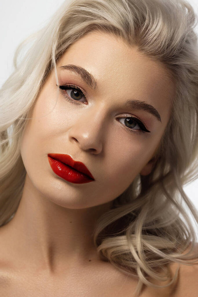 Close-up beauty of a female face with fashion evening make-up. Black liner on the eyes and extremely long eyelashes, on full lips matte scarlet lip color. Well-groomed skin after spa. red lipstick - Photo, Image