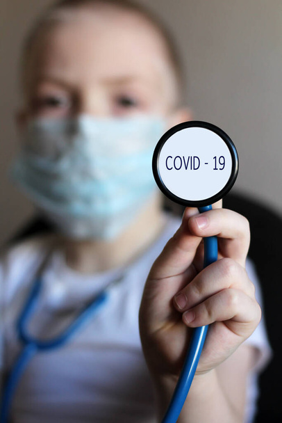 A little boy in a medical mask with a stethocope, on a gray background. Concept of medicine and healthcare in the fight against viruses. Children against coronavirus. So close. - Foto, Imagem