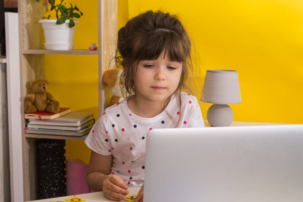 Online okul. Küçük kız dizüstü bilgisayar kullanıyor. Uzaktan eğitim ya da uzaktan öğrenme. Çocuk kız oturma odasında internetten ders çalışıyor. Covid-19 Coronavirüs. - Fotoğraf, Görsel