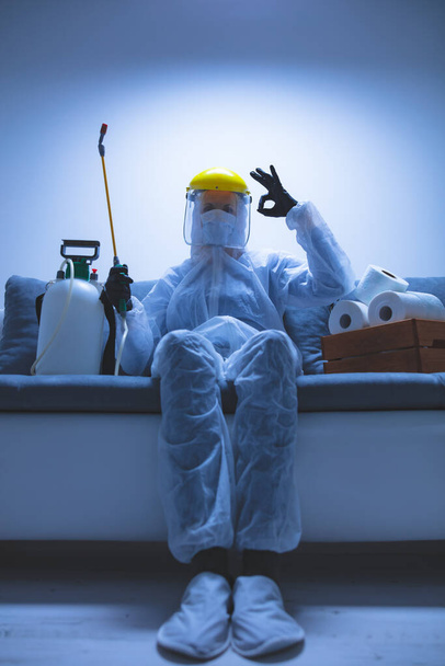 Scientist with protective suit and face mask, bio hazard sprayer for decontamination agaist viruses, germs - toilet paper stock paranoia at home, waiting for end of days. - Photo, Image