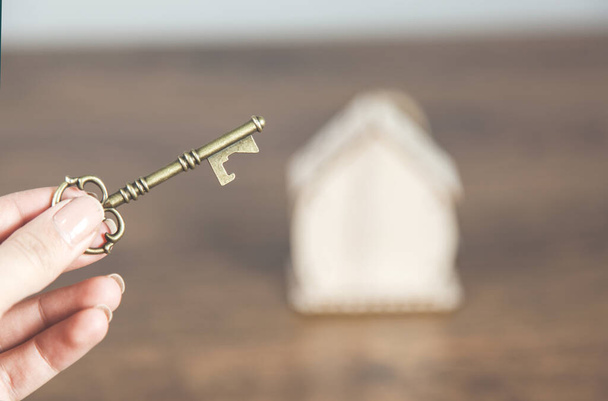 vrouw hand sleutel en huis model op bureau - Foto, afbeelding