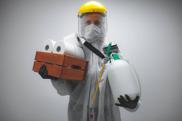 Person scientist with protective suit and face mask, bio hazard sprayer for decontamination agaist viruses, germs - toilet paper stock paranoia at home, waiting for end of days. - Photo, Image