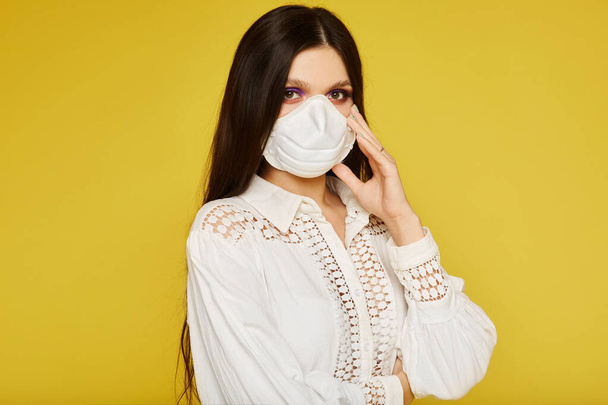 Portrait of a young woman wearing a protective face mask, looking at the camera, close up, isolated on yellow background. Flu epidemic, dust allergy, air pollution concept. Healthcare concept - Zdjęcie, obraz