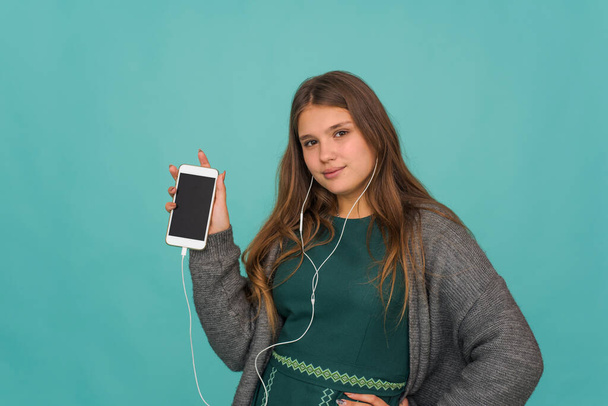 Fashion pretty sweet carefree teenage girl listening music in headphones and singing with smartphone over blue background - Photo, Image