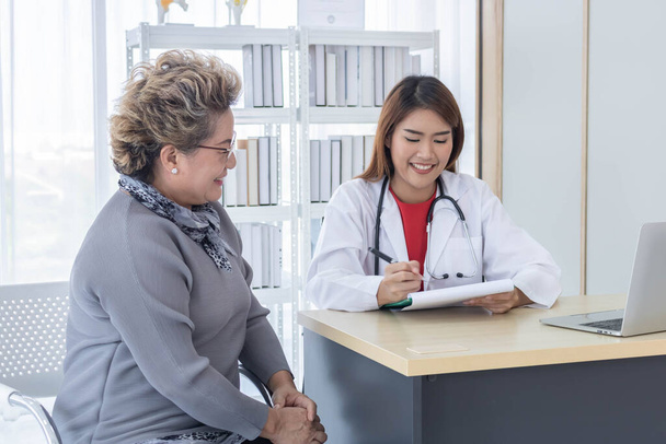 Азиатский врач работает в офисе и обсуждает с пациентом ее симптомы, лечение и концепцию больницы
. - Фото, изображение