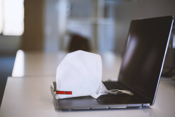 Quarantined work items. Home office. Laptop and medical mask on the office desk - Photo, Image