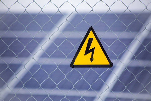 Industrial solar power farm station on background selective focus on yellow triangular high voltage warning sign. Electricity concept. - Photo, Image