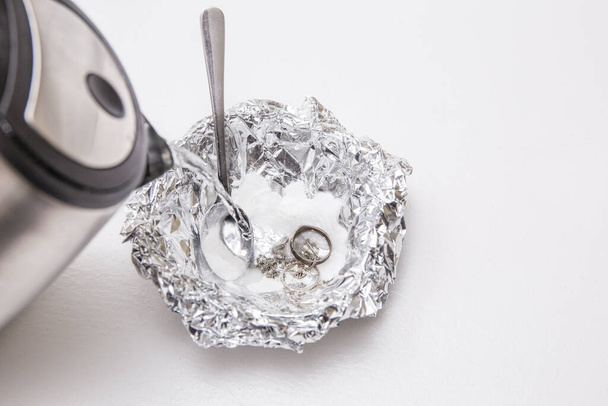 A solution of baking soda(Sodium bicarbonate) and warm water will remove the tarnish from silver when the silver is in contact with a piece of aluminium tin foil. Pouring hot water over silver. - Photo, Image