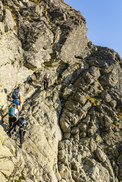 Tatranska Polianka, Eslovaquia - 01 de septiembre de 2019: El guía de montaña protege a los turistas que escalan en Velicka Proba (Wielicka Proba), que conduce al pico Gerlach (Gerlachov) en las montañas Tatra.
. - Foto, Imagen