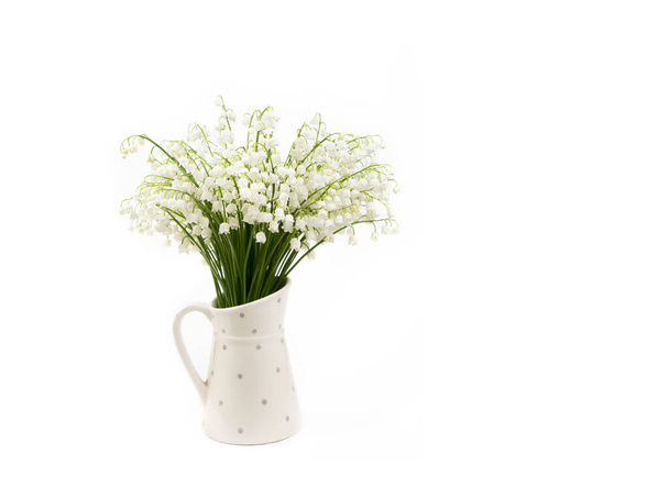 Boeket witte bloemen Lily van de vallei (Convallaria majalis) ook wel: Mei klokken, Onze Lieve Vrouw tranen en Maria 's tranen in een witte gestippelde kruik vormige vaas geïsoleerd op wit. - Foto, afbeelding