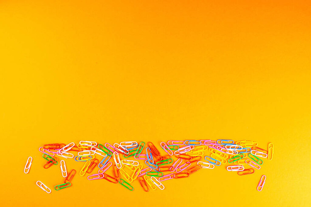 A pile of colored paper clips scattered on a orange surface. - Фото, изображение