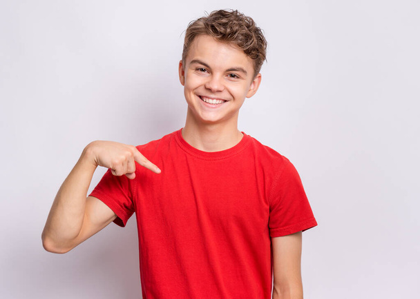 Portrait of handsome teen boy pointing oneself, on grey background. Emotions and signs concept. Happy smiling child looking at camera. Young student points fingers at himself - Valokuva, kuva
