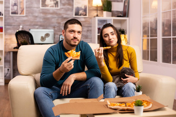 Hermosa pareja joven comiendo pizza mientras ve la televisión
 - Foto, Imagen