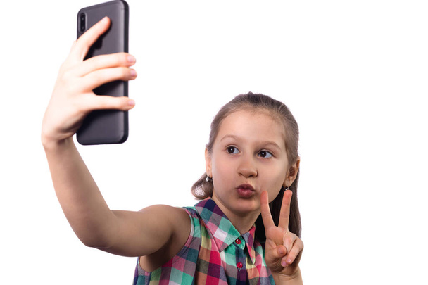 Cute little girl taking a selfie on her phone. Studio photo on white background - Fotografie, Obrázek