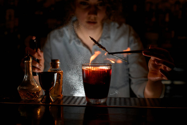 Professional woman barman decorates red cocktail, sprinkles on it and makes fire. - Φωτογραφία, εικόνα