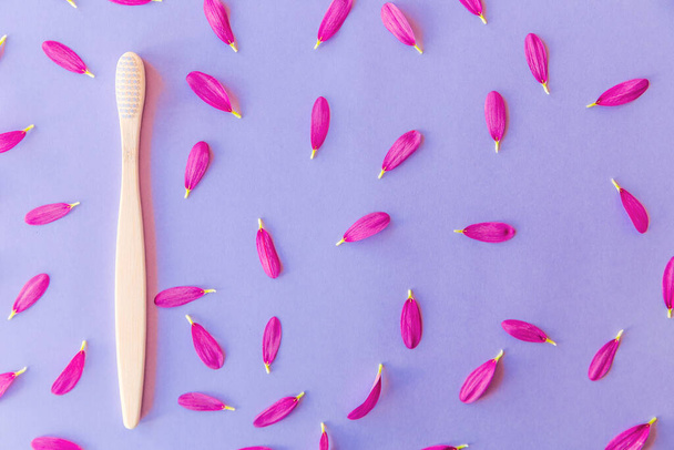 White wooden toothbrushes on violet or purple background with petals. Top view - Photo, Image