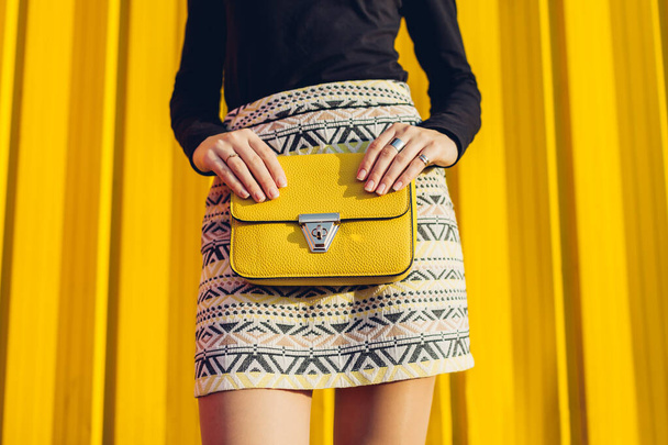 Moda. Mujer joven sosteniendo bolso amarillo elegante bolso con mini falda al aire libre. Primavera ropa femenina y accesorios
. - Foto, imagen