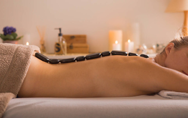 Mujer joven recibiendo masaje de piedra caliente en el salón de spa. Concepto de tratamiento de belleza. La chica se relaja en los procedimientos de spa - Foto, Imagen
