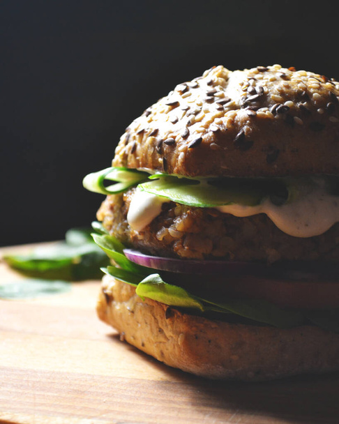 vegan burger με φαγόπυρο, ντομάτα, κρεμμύδι, μαγιονέζα vegan και σπανάκι σε ένα φρέσκο κουλούρι με λιναρόσπορο και σουσάμι, περιτριγυρισμένο από φύλλα σπανάκι - Φωτογραφία, εικόνα