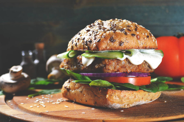 veggie, vegan burger with buckwheat, tomato, onion, vegan mayonnaise and spinach on a fresh bun with flax seeds and sesame, surrounded by spinach leaves, mushrooms, tomato, black pepper and spices. - Foto, imagen