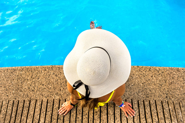 Top lefelé néző fiatal nő visel sárga szalma kalap pihen közelében medence tiszta kék víz a nyári napsütéses napon. - Fotó, kép