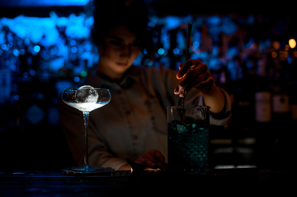 donna al bar scuro mescola cocktail in grande vetro con cucchiaio
. - Foto, immagini