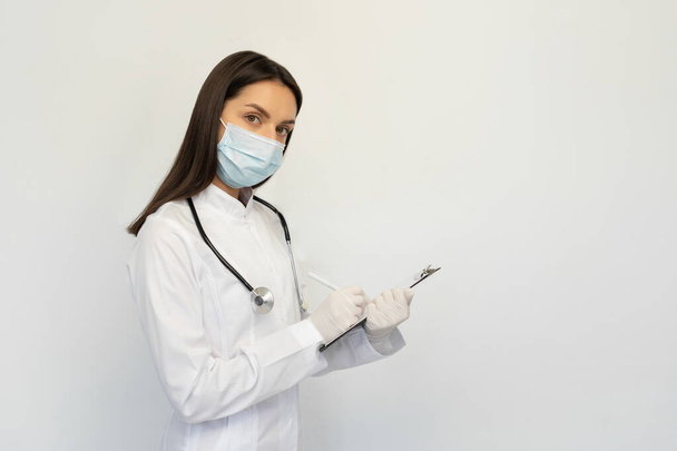 Femme médecin dans un masque médical de protection et des gants, écrit le diagnostic à la carte des clients
 - Photo, image