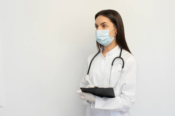 Kobieta lekarz w ochronnej masce medycznej i rękawiczki, pisze diagnozę do karty klienta - Zdjęcie, obraz