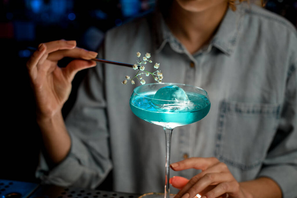 Primer plano. Señora camarera decora vidrio con rama de flor de bebida azul
. - Foto, imagen
