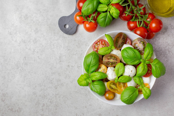 Italian, traditional caprese salad with cherry tomatoes, mozzarella and basil. Salad ingredients, olive oil, spices, salt. Organic and natural food concept. Light background. Top view. Copy space. - Foto, Bild