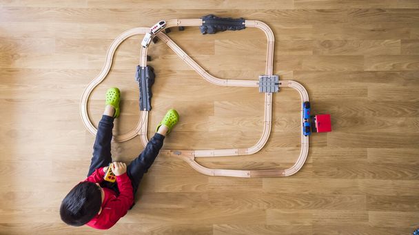 nierozpoznawalny chłopiec bawi się drewnianym pociągiem i zdalnym sterowaniem na drewnianej podłodze salonu, podczas gdy jest ograniczony do koronawirusu - Zdjęcie, obraz