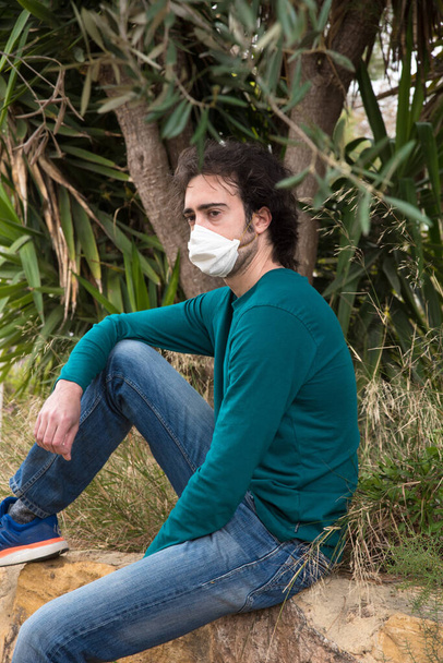 マスクを身に着けているコロナウイルスによる隔離で若い男は庭でしばらく過ごす - 写真・画像