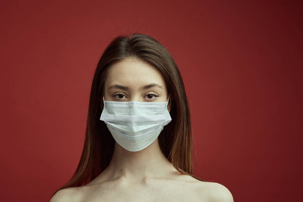A young girl in a medical mask on a red background. Poster about the coronavirus COVID-19 pandemic. - Foto, imagen