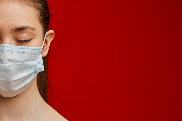 A young girl with closed eyes in a medical mask on a red background. Poster about the corona virus COVID-19 pandemic. - Fotó, kép