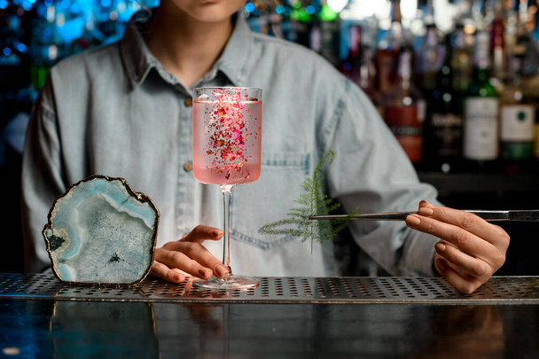 Lady barman beginnen te glas versieren met rozencocktail door stuk van groene plant. - Foto, afbeelding
