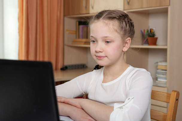 Serious schoolgirl looks at a laptop screen. Distance learning online education, home school, home education, quarantine concept - Image - Zdjęcie, obraz