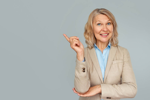 Portrait of business woman pointing up and looking at the camera over gray background . - Fotoğraf, Görsel
