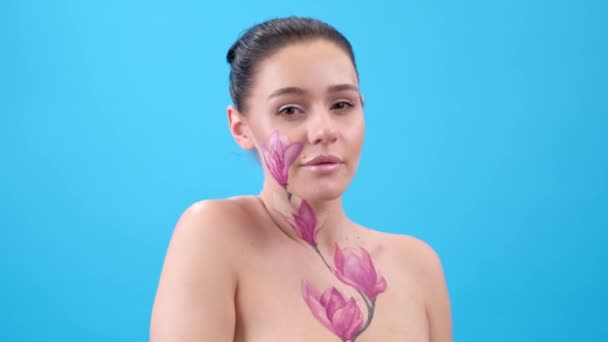 Body Art: Frau mit bemalter Magnolie im Gesicht und Brustkorb. Blume auf Körper. Blauer Hintergrund - Filmmaterial, Video