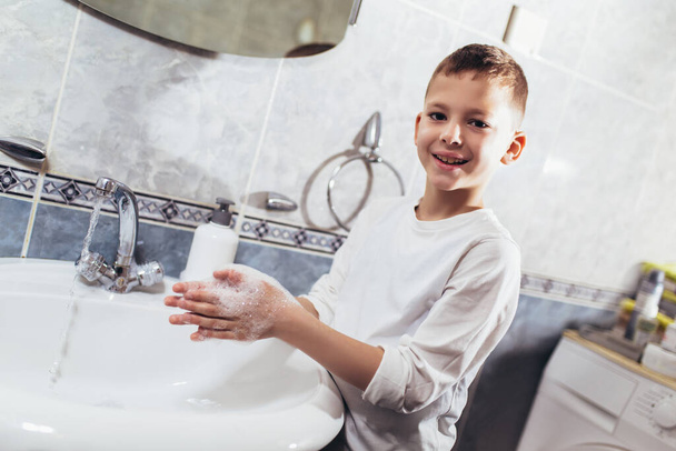 Leuke jongen die zijn handen wast in de badkamer. Bescherming tegen virussen en bacteriën. - Foto, afbeelding
