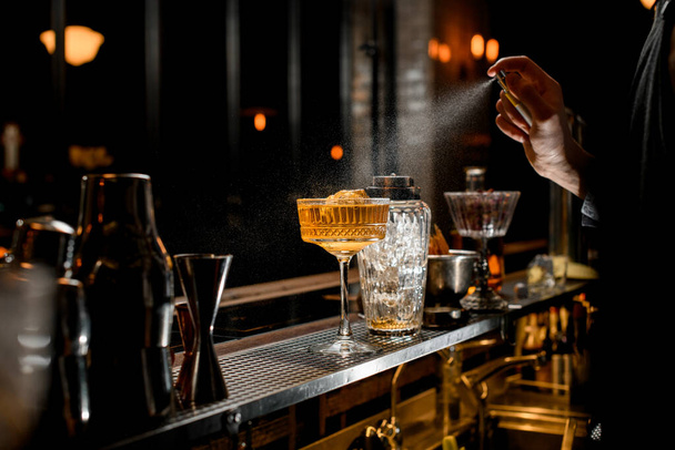 Barman v černé zástěře energicky sype na sklo s koktejlem. - Fotografie, Obrázek