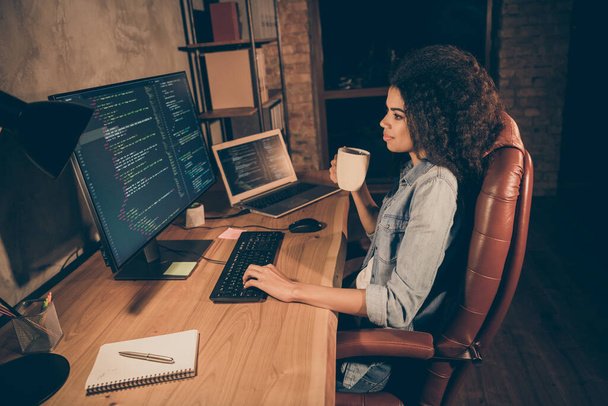 Profile side photo professional dark skin girl web administrator sit evening desk want pause she need work framework operating system research hold drink mug beverage in workplace workstation - 写真・画像