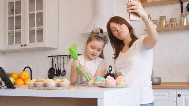 Äiti ja tytär kuorrutus cupcakes ja ottaa videopuhelu
 - Valokuva, kuva