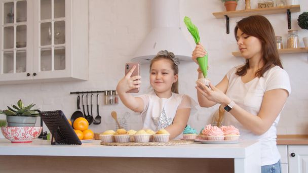 Мати і дочка глазурують кекси і мають відеодзвінок
 - Фото, зображення