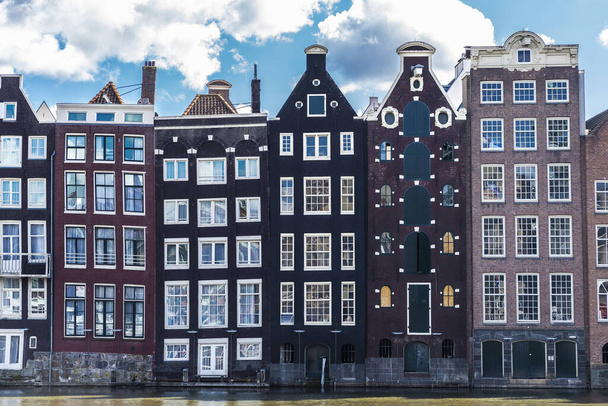 Velhas casas tradicionais inclinadas ao longo de um canal em Damrak Waterfront, Amsterdã, Países Baixos
 - Foto, Imagem