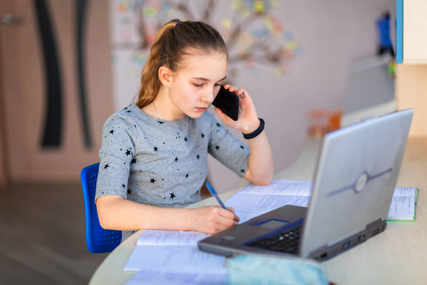 Beautiful young school girl working at home in her room with a laptop and class notes studying in a virtual class. Distance education and learning, e-learning, online learning concept during quarantine - Zdjęcie, obraz